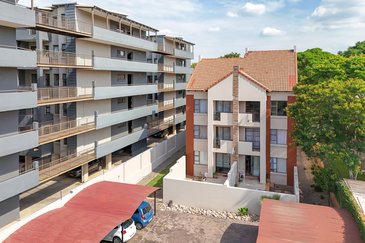 Aerial view of an apartment complex featuring multi-story residential buildings, paved parking areas with carports, and established surrounding greenery.