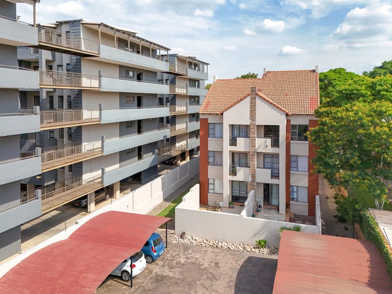 Aerial view of an apartment complex featuring multi-story residential buildings, paved parking areas with carports, and established surrounding greenery.