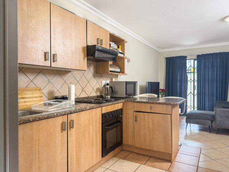 Open-plan kitchen featuring laminate cabinetry, granite countertops, and built-in appliances, flowing into a living area with access to a patio through a security gate.
