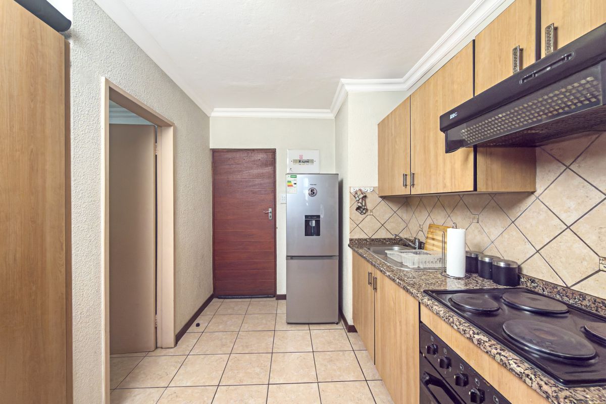 A functional kitchen featuring light wood cabinetry, granite countertops, a built-in oven with hob, and tiled flooring throughout.