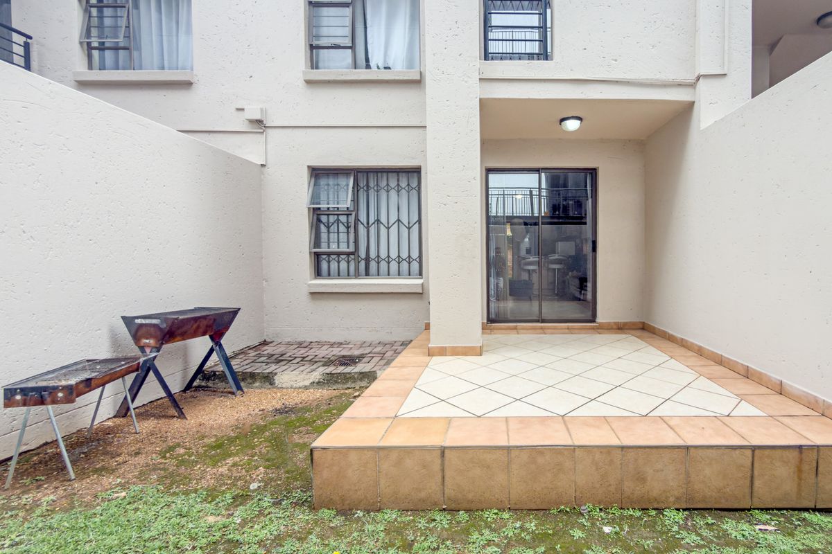 Rear exterior view of the apartment featuring a tiled patio area, sliding glass door access, and security bars on windows.