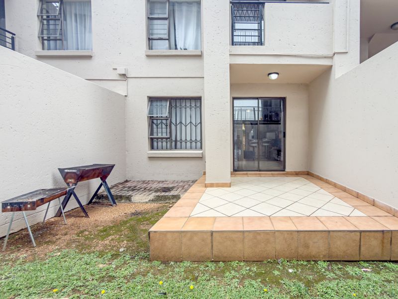 Rear exterior view of the apartment featuring a tiled patio area, sliding glass door access, and security bars on windows.
