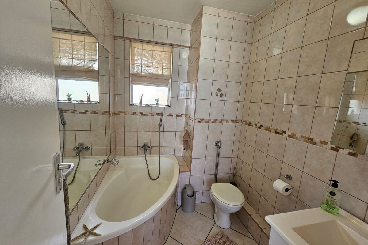 A functional bathroom featuring a corner bathtub with handheld shower, wall-mounted toilet, and a vanity basin with large wall mirror.