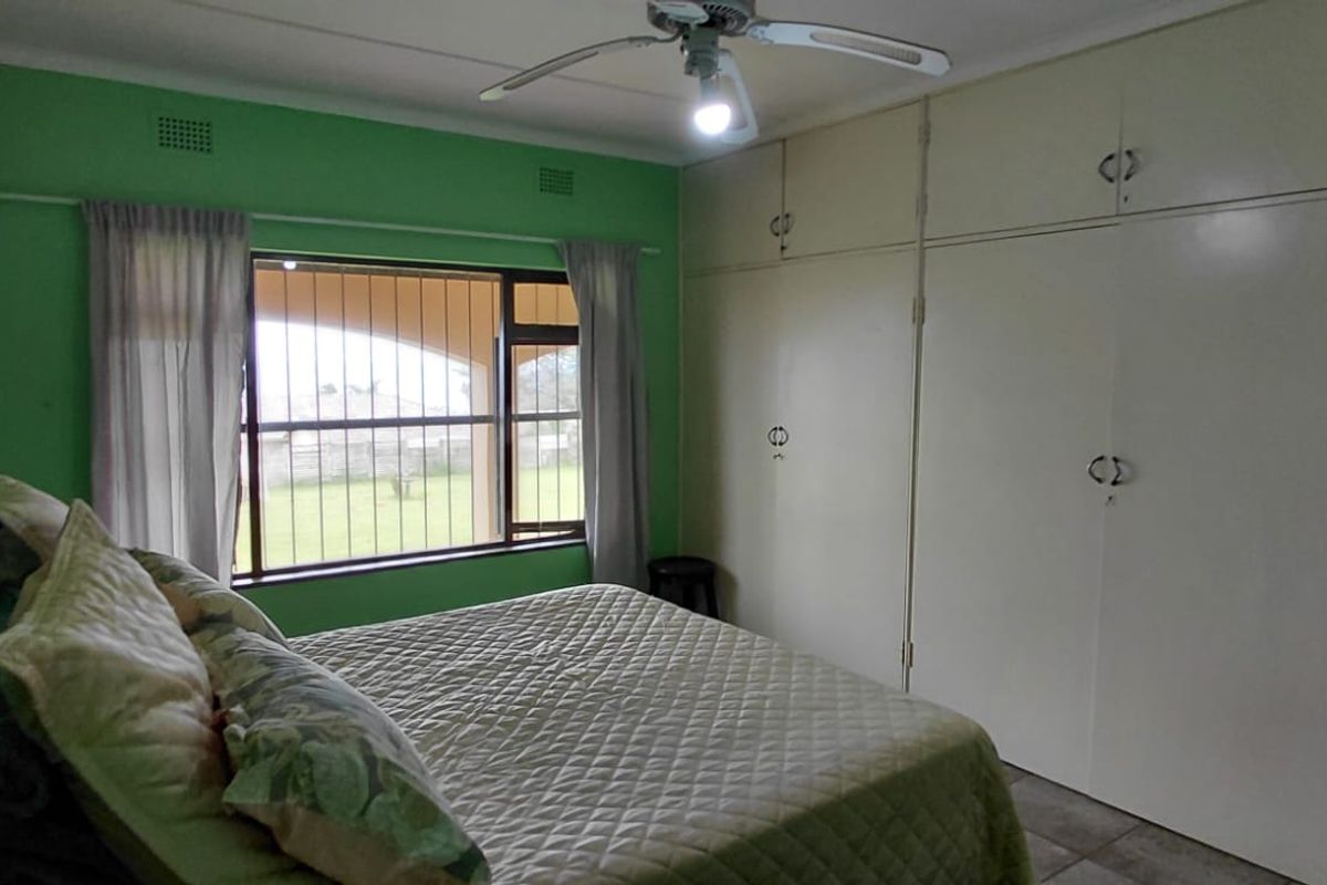 A bedroom featuring built-in floor-to-ceiling cupboards, a ceiling fan, and a window with security bars overlooking the garden.