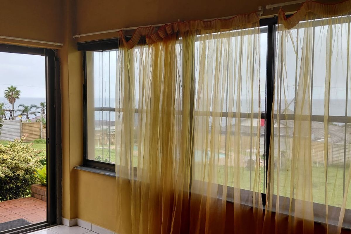 A sunroom or living area featuring large windows with views of the garden and ocean, providing natural light and direct access to the patio.