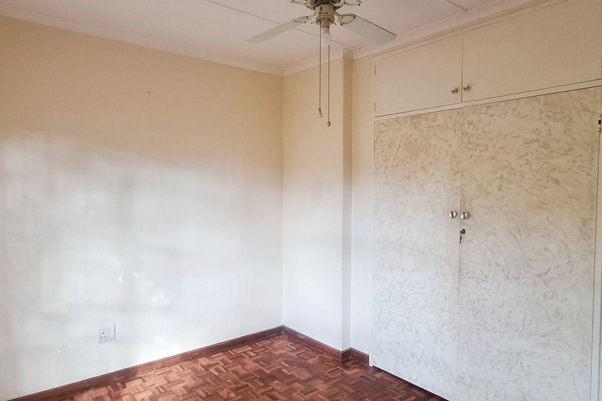 A clean, empty bedroom featuring classic parquet flooring, built-in cupboards with overhead storage, a ceiling fan, and an installed air conditioning unit.