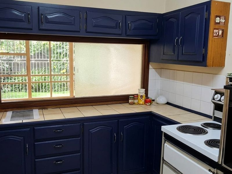 Kitchen featuring dark blue built-in cabinetry, tiled countertops, a tiled backsplash, and an electric stove with a view through a sliding window.