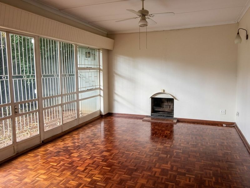 Spacious living room featuring classic parquet flooring, a built-in fireplace, and large glass sliding doors that provide ample natural light and garden access.