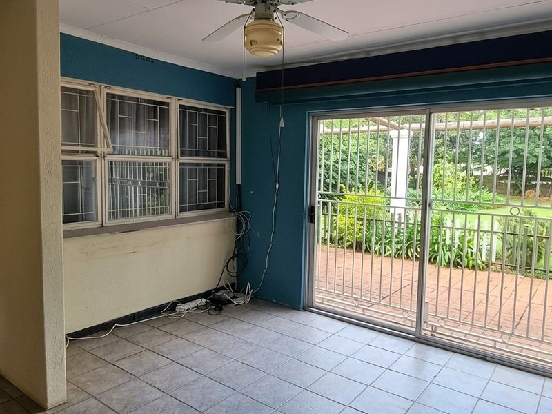 An empty living room featuring tiled flooring, a ceiling fan, and a sliding glass door providing access to the outdoor patio area.