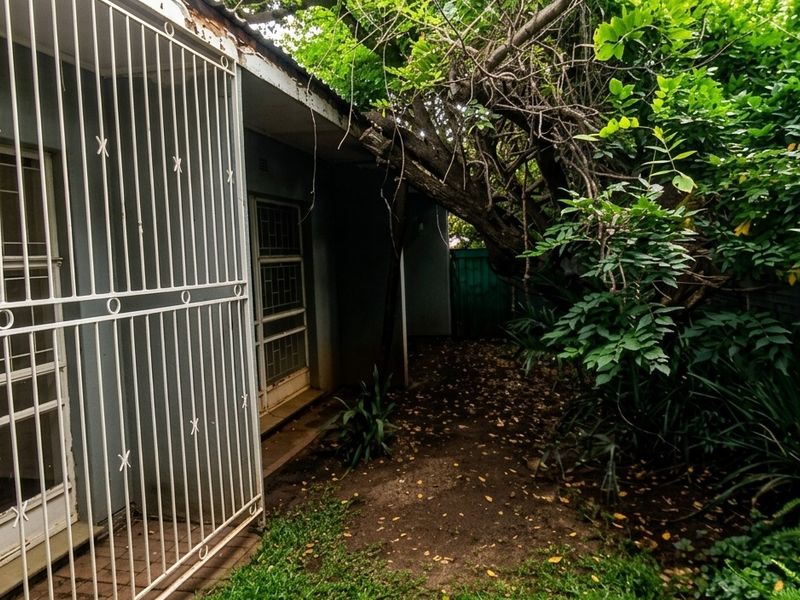 A view of the rear exterior of the house featuring security bars on windows and doors, with overgrown garden foliage adjacent to the building structure.
