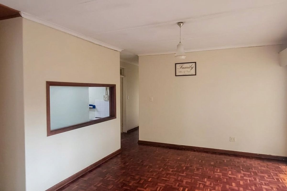 Spacious living area featuring classic parquet flooring, a convenient serving hatch to the kitchen, and large windows with security gates.