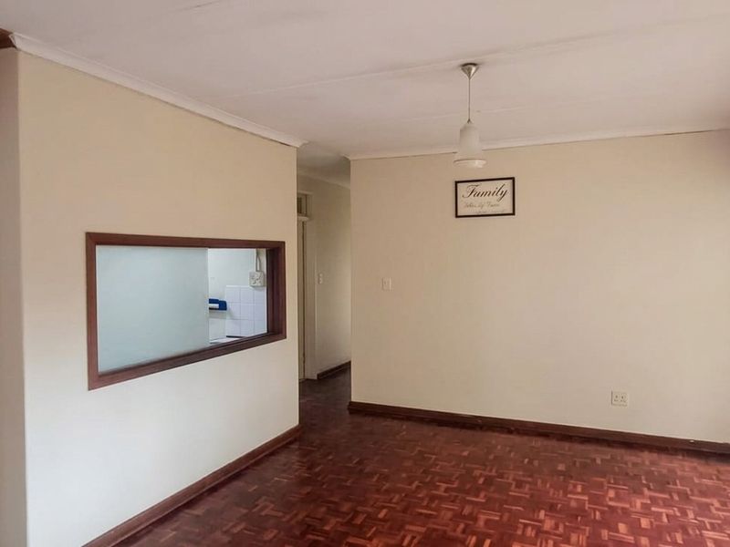 Spacious living area featuring classic parquet flooring, a convenient serving hatch to the kitchen, and large windows with security gates.
