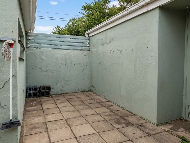 A paved rear courtyard area featuring exterior walls with visible plaster cracking and a window with security bars.