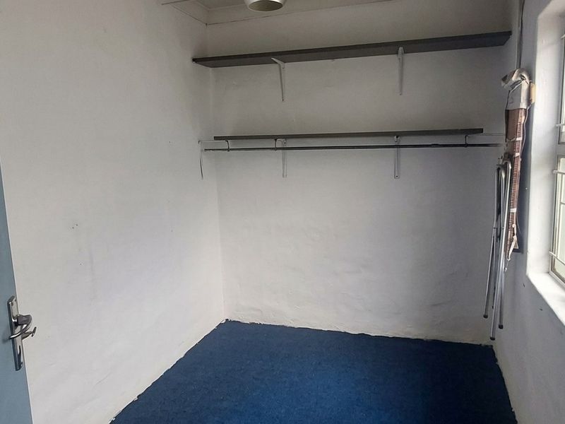 A functional laundry room featuring built-in shelving, a window with security bars, and direct access via an internal door.