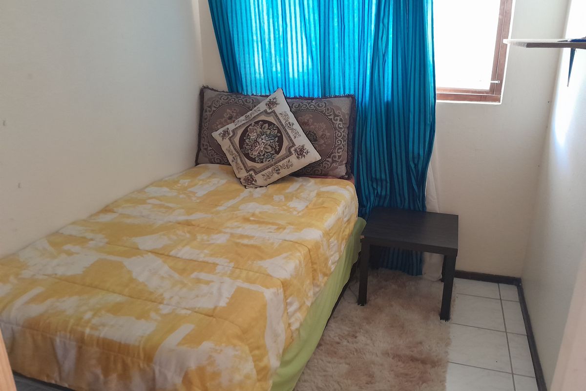 A compact bedroom featuring tiled flooring and a window with blue curtains, suitable for a single bed or home office setup.