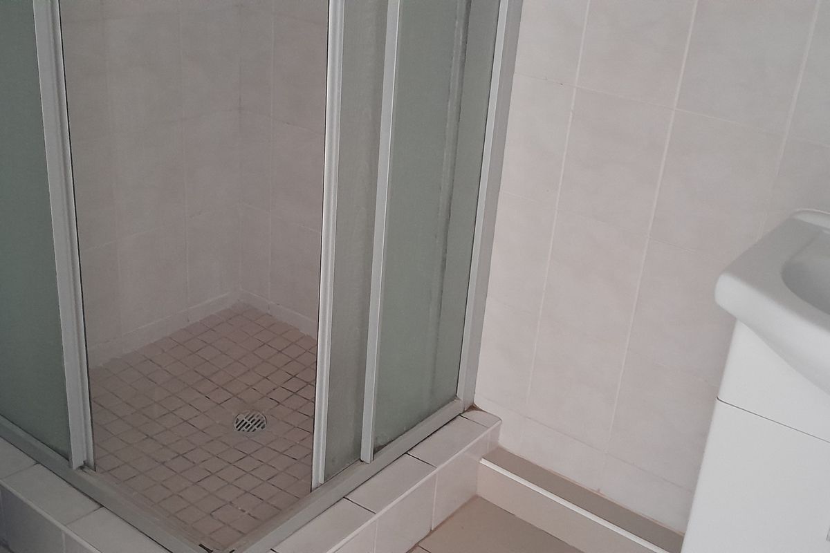 Compact bathroom featuring a corner shower enclosure with sliding doors, a pedestal vanity basin, and tiled wall surfaces.