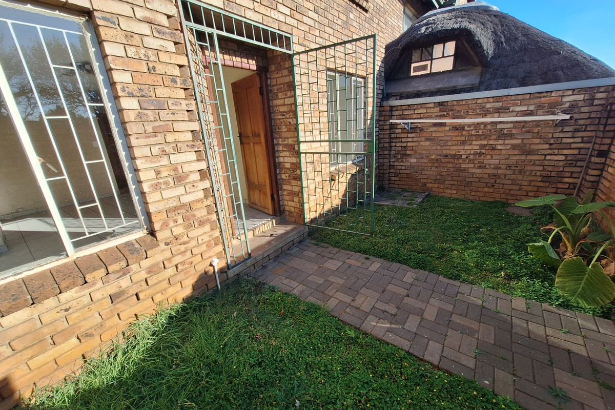 Rear exterior view of the townhouse featuring face brick construction, a paved walkway, security gates, and a section with a thatched roof.