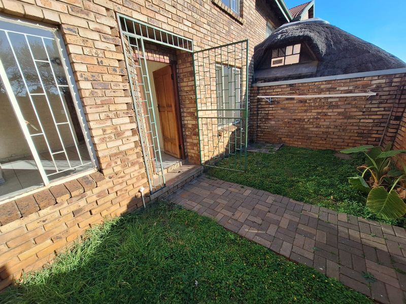 Rear exterior view of the townhouse featuring face brick construction, a paved walkway, security gates, and a section with a thatched roof.