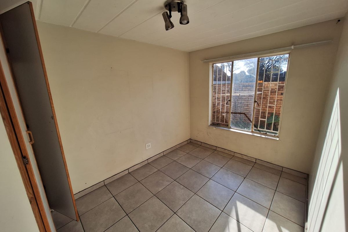 An empty bedroom featuring tiled flooring, a built-in cupboard, and a window fitted with security bars.