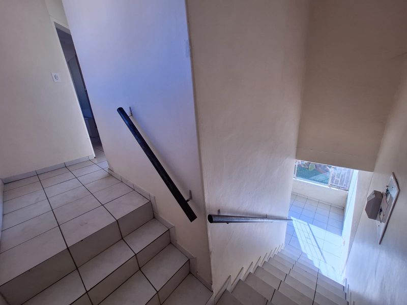 A functional tiled staircase with metal handrails connecting levels, featuring neutral wall finishes and natural light from a landing window.