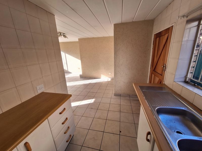 An empty kitchen area featuring tiled flooring, built-in cabinetry with laminate countertops, a stainless steel sink, and a timber door leading to the exterior.