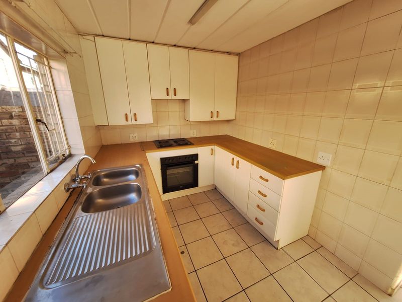 A functional, dated kitchen featuring built-in cabinetry, a double sink, and integrated oven and hob, offering a blank canvas for modern renovation.