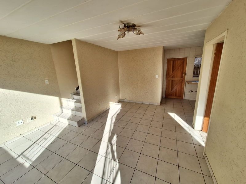 An empty living area featuring tiled flooring, a staircase, and textured walls, offering a blank canvas for renovation and interior design updates.
