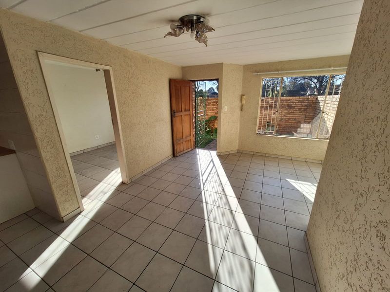 An empty living room featuring tiled flooring, textured walls, and direct access to an outdoor area through a timber door.