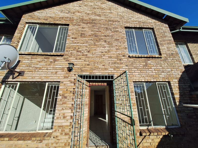 Front elevation of a double-story face brick townhouse featuring security gates, burglar bars, and a tiled roof.