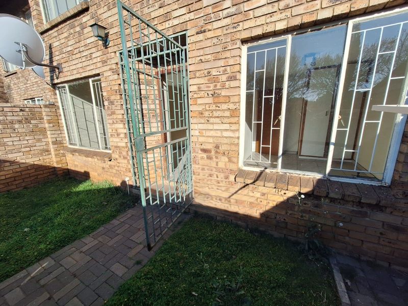 Rear exterior view of the townhouse featuring face brick construction, security gates, and a paved walkway leading to the entrance.