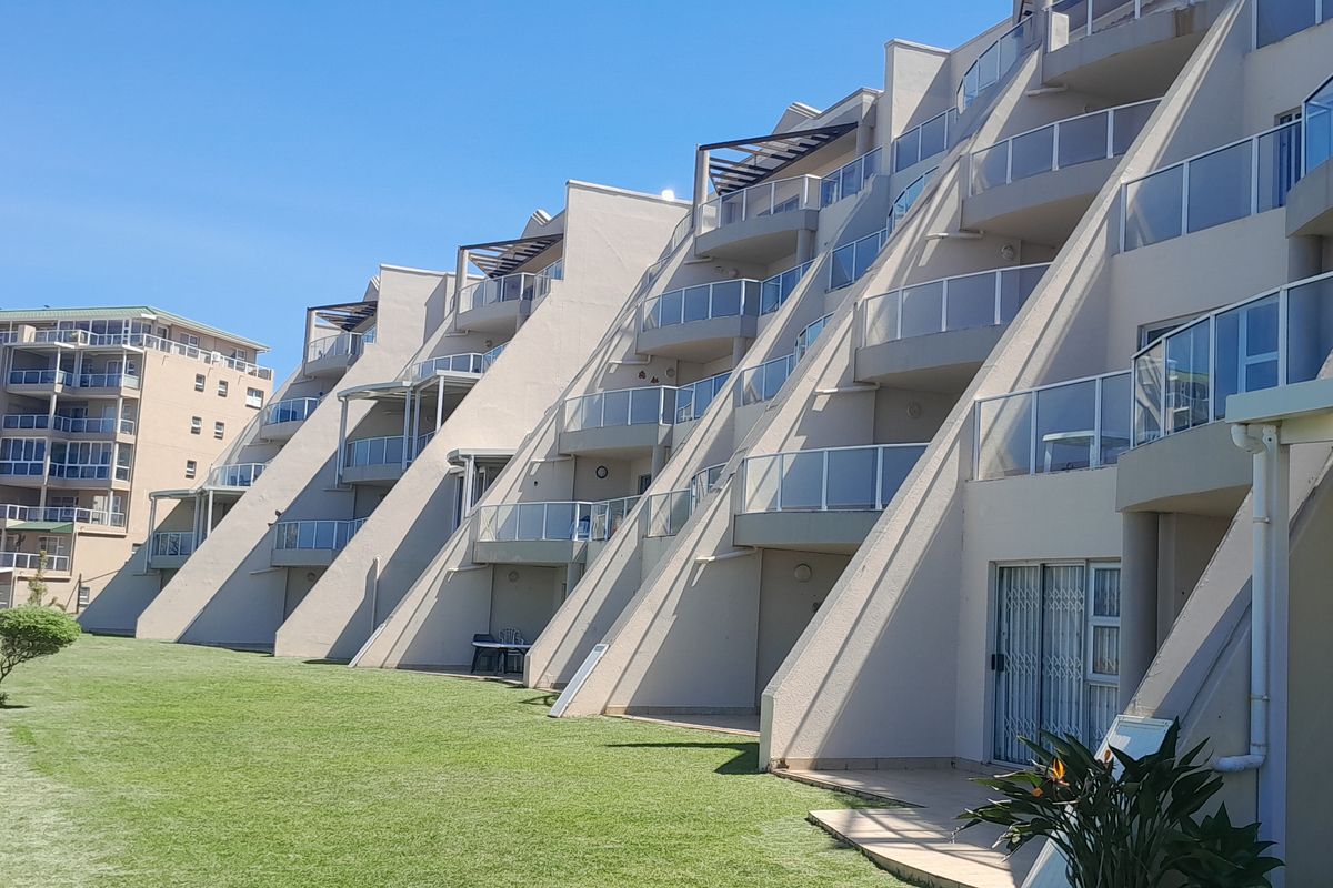 A view of the rear elevation of a multi-story apartment complex featuring tiered balconies with glass balustrades and ground-floor patio access to a lawn.