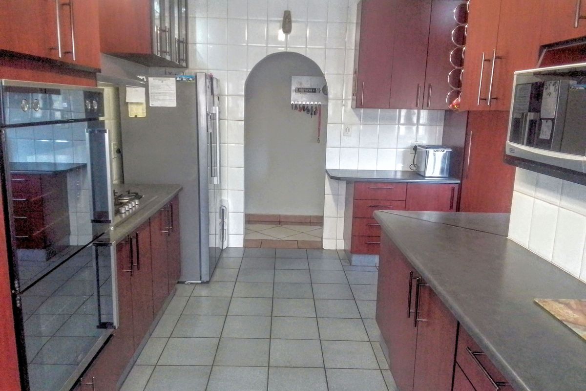A functional kitchen featuring dark wood-look cabinetry, tiled splashbacks, built-in oven, gas hob, and tiled flooring with an arched doorway leading to an adjacent space.