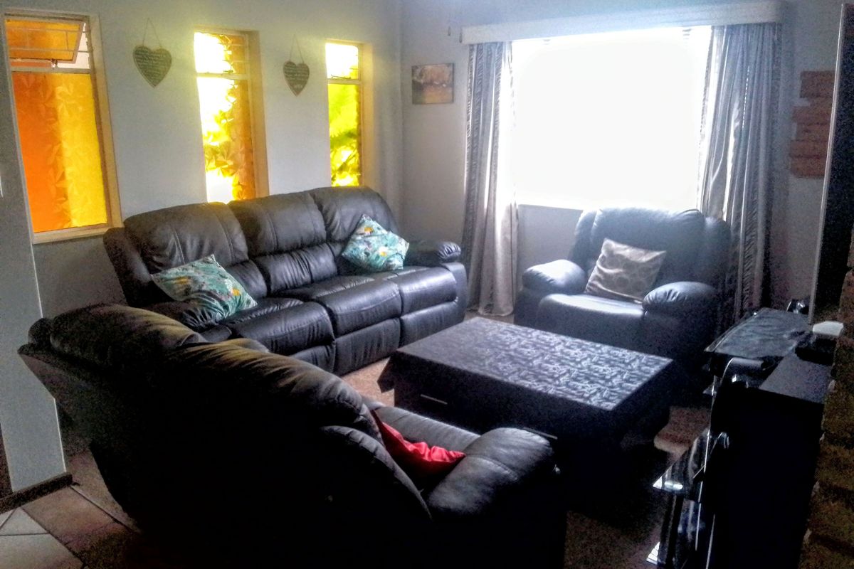 A living room featuring tiled flooring and multiple windows, providing natural light to the seating area.