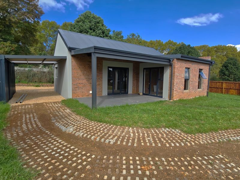 Modern single-story home featuring a brick and plaster facade, corrugated metal roof, covered patio area, and a paved driveway with an attached carport.