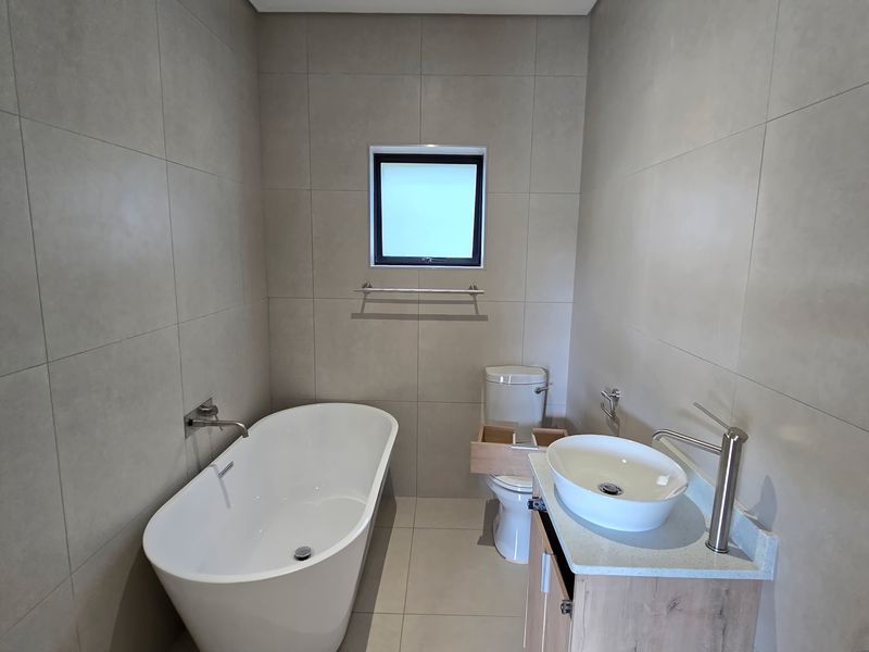 Modern bathroom featuring a sleek freestanding bathtub, vessel sink vanity, and neutral floor-to-ceiling tiling.