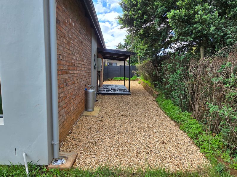 A side exterior view of the property featuring a brick facade, gravel pathway, and a small covered patio area.