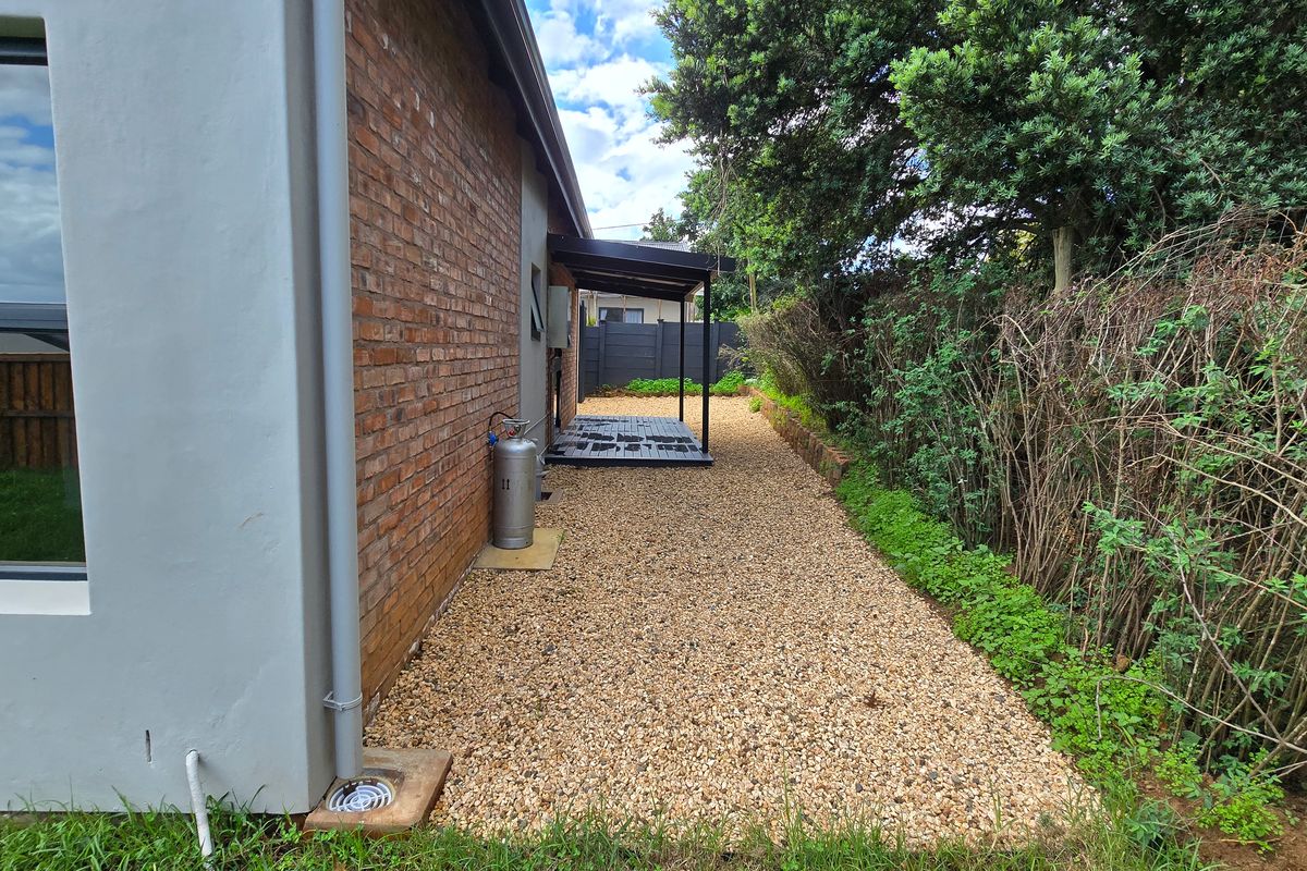 A side exterior view of the property featuring a brick facade, gravel pathway, and a small covered patio area.