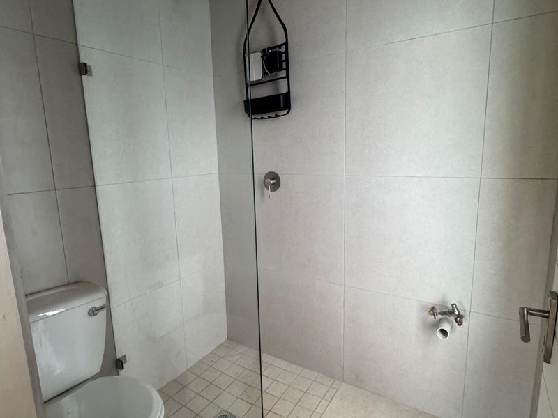 A modern bathroom featuring a glass-enclosed walk-in shower with a rain shower head and neutral wall and floor tiling.