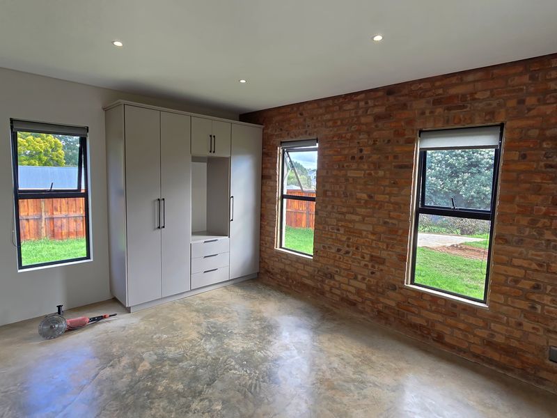 A modern bedroom featuring an exposed brick wall, polished concrete floors, built-in cabinetry, and large windows providing natural light.