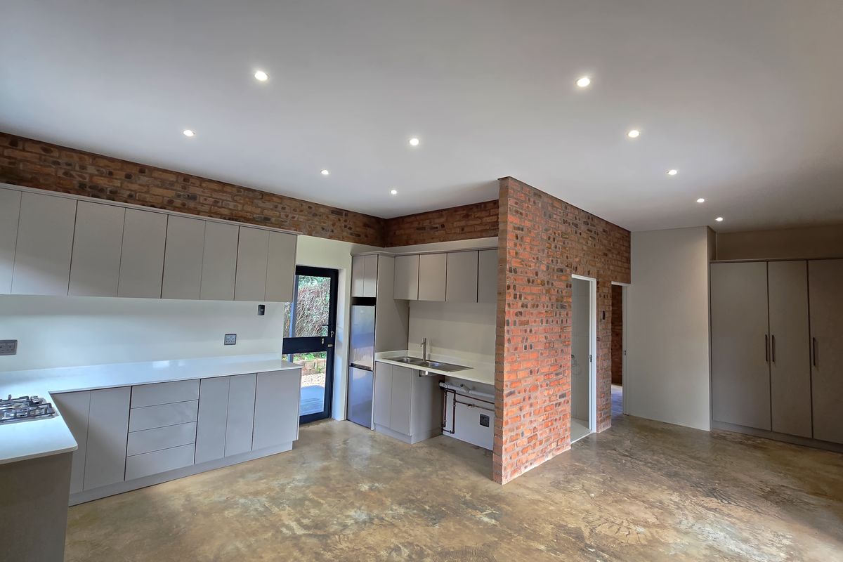 Modern kitchen featuring sleek cabinetry, stone countertops, gas hob, and exposed brick walls, set against polished concrete flooring with recessed lighting.