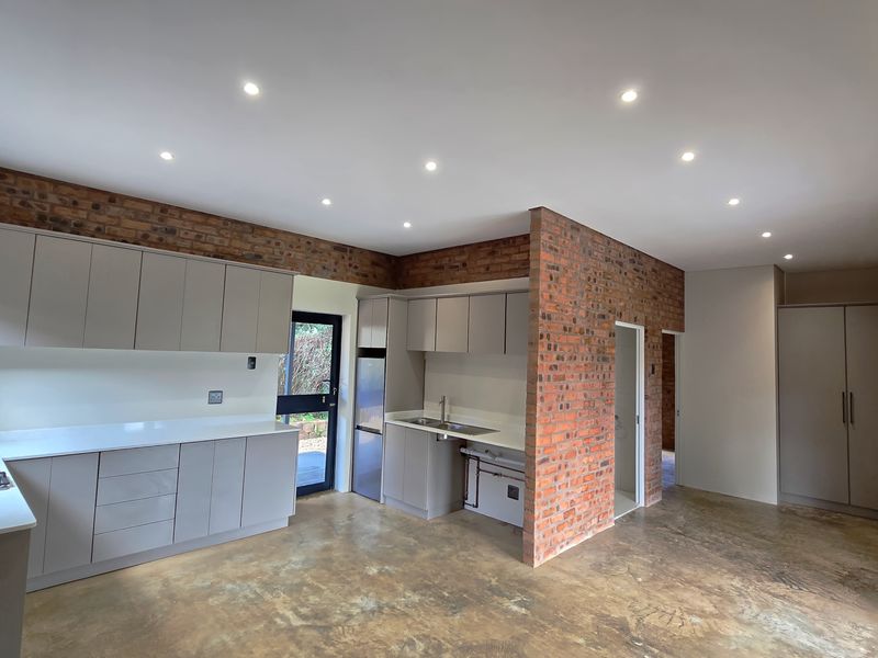 Modern kitchen featuring sleek cabinetry, stone countertops, gas hob, and exposed brick walls, set against polished concrete flooring with recessed lighting.