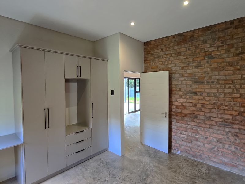 Modern bedroom featuring a polished concrete floor, exposed brick feature wall, and integrated built-in cabinetry with a desk area.