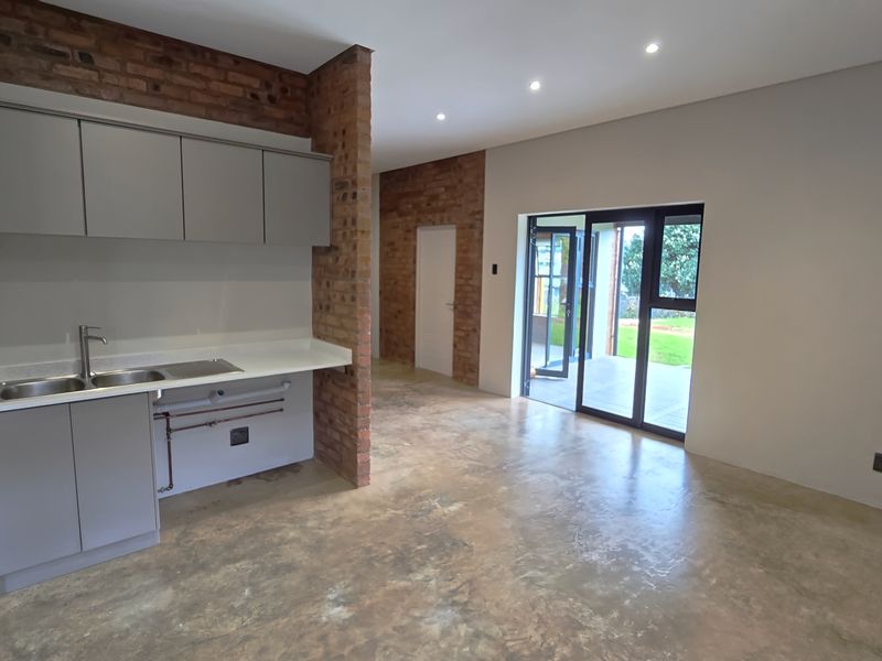 Modern open-plan living area featuring polished concrete floors, exposed brick accents, and a sleek kitchen with built-in cabinetry and direct patio access.