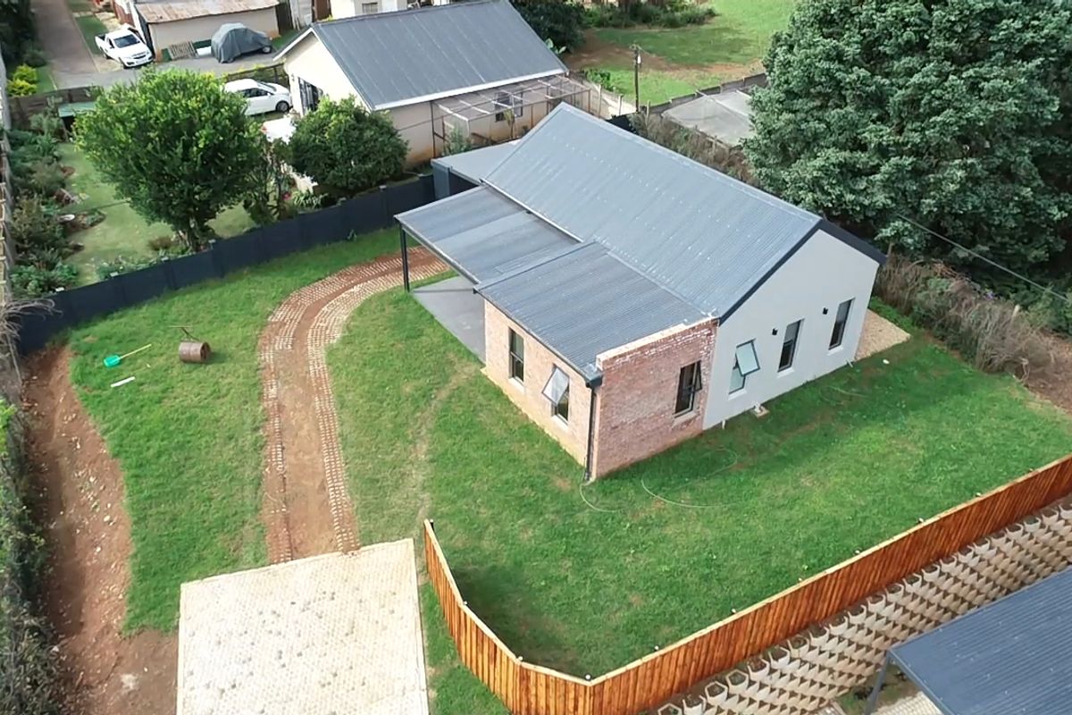 Aerial view of a residential property featuring a combination of brick and plastered exterior walls, a metal roof, and a well-maintained garden with paved pathways.