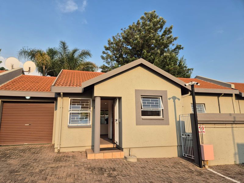 Front elevation of a townhouse featuring a tiled roof, paved driveway, integrated garage, and security features including window bars and a mounted camera.