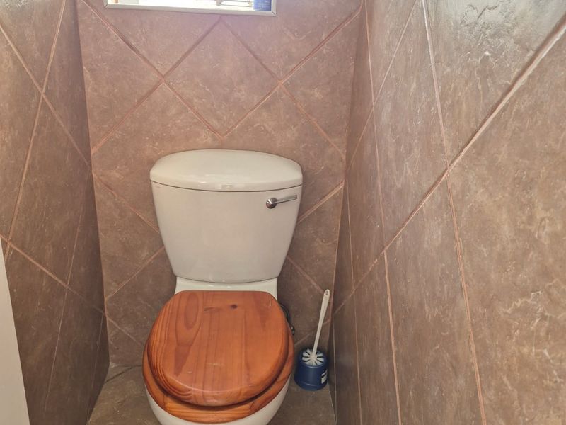 A compact bathroom featuring full-height wall tiling, tiled flooring, and a standard toilet with a window for natural light.