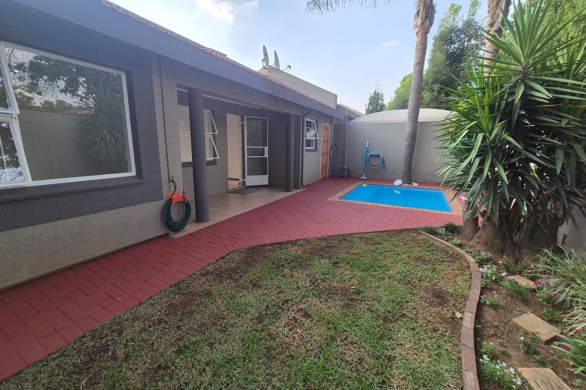Rear exterior view of the townhouse featuring a paved patio area, a small swimming pool, and a landscaped garden bed.