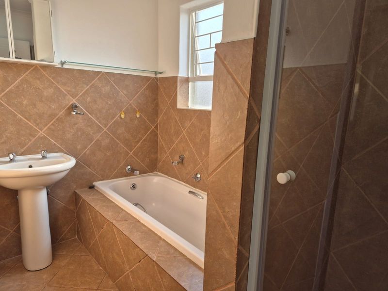 A functional bathroom featuring a pedestal basin, a built-in bathtub with tiled surround, and a separate shower enclosure.
