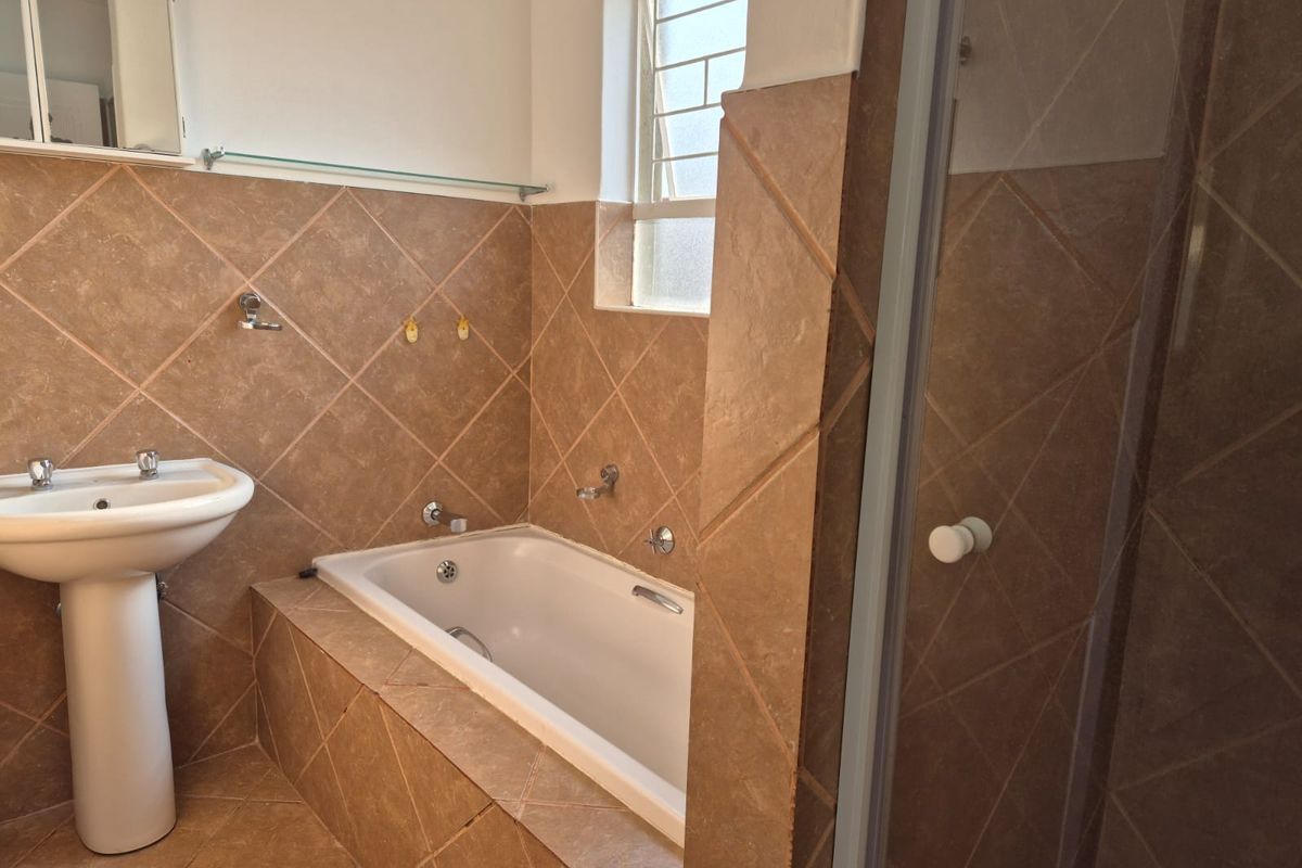 A functional bathroom featuring a pedestal basin, a built-in bathtub with tiled surround, and a separate shower enclosure.