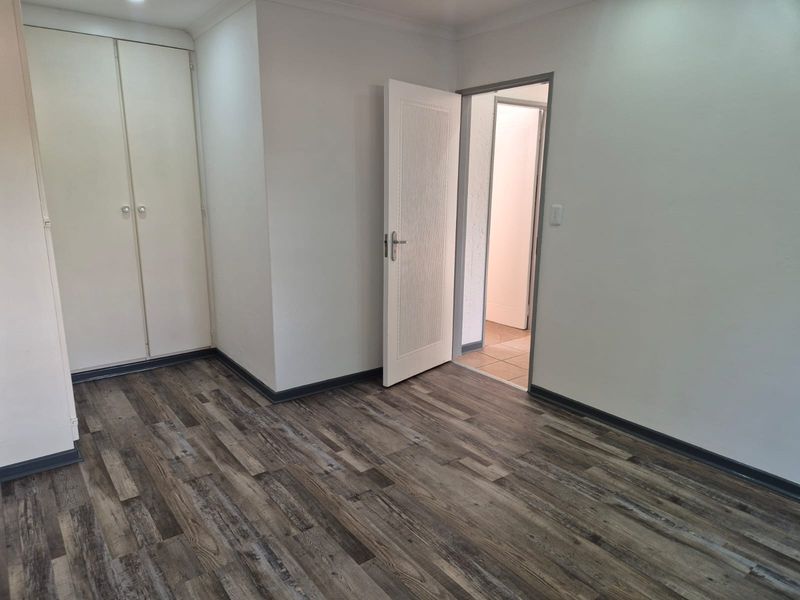 An empty bedroom featuring modern wood-look laminate flooring, built-in cupboards, and neutral wall finishes, providing a clean and versatile living space.